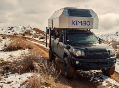 A truck with a Kimbo trailer drives down a snowy red dirt road.