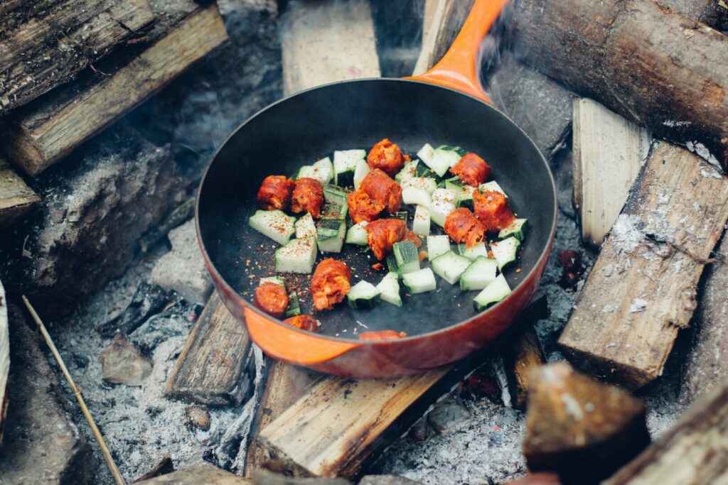 Vegetables cooking in a cast iron skillet over a fire while camping.