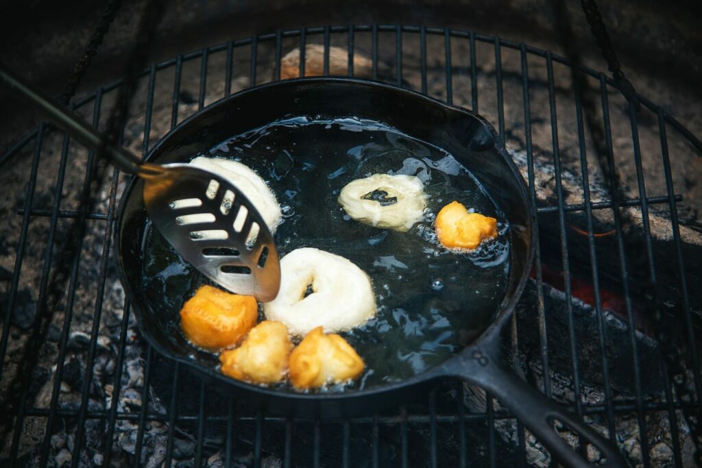 Camp fire donuts being made in a cast iron skillet over the fire.