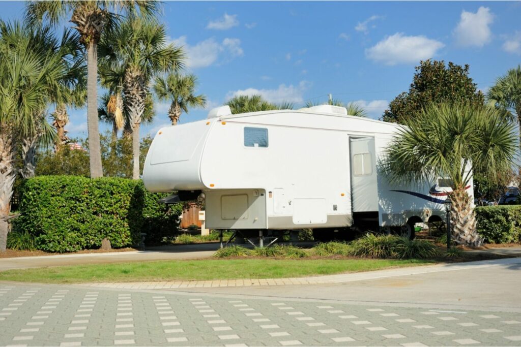 A fifth parked at an RV resort with manicured campsites surrounded with palms and decorated paver driveways.