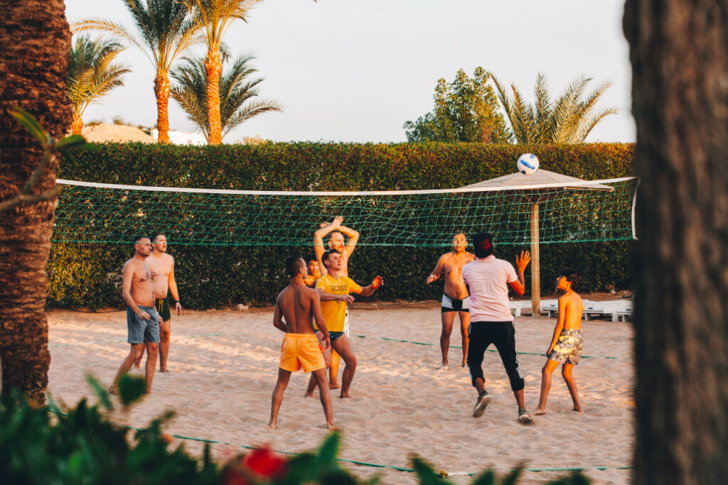 A group of men playing beach volleyball at sunset.