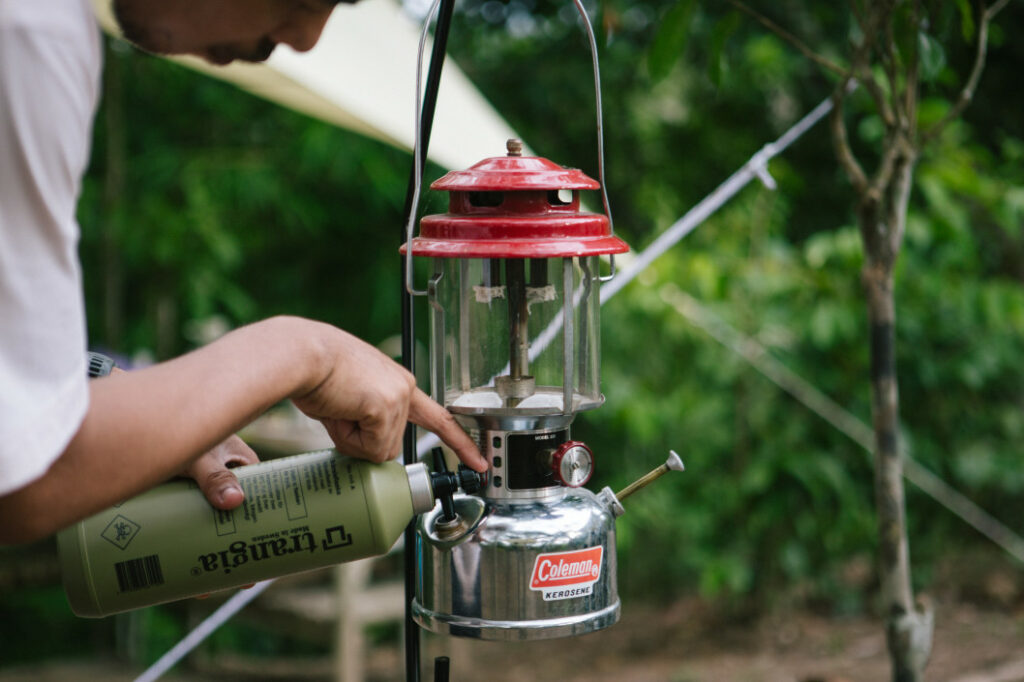 A camper fills a Coleman kerosene lantern to light his campsite.