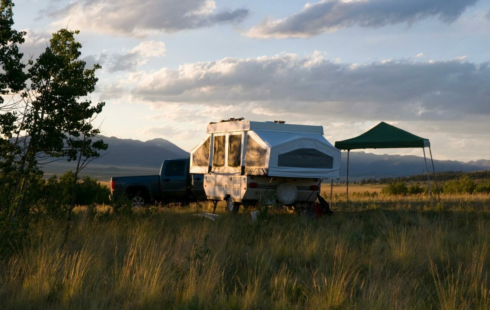 A pop-up camper camps out in a field next to its tow vehicle and canopy