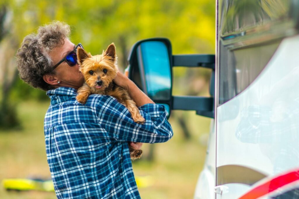 A woman cuddles her small dog in her arms beside her RV