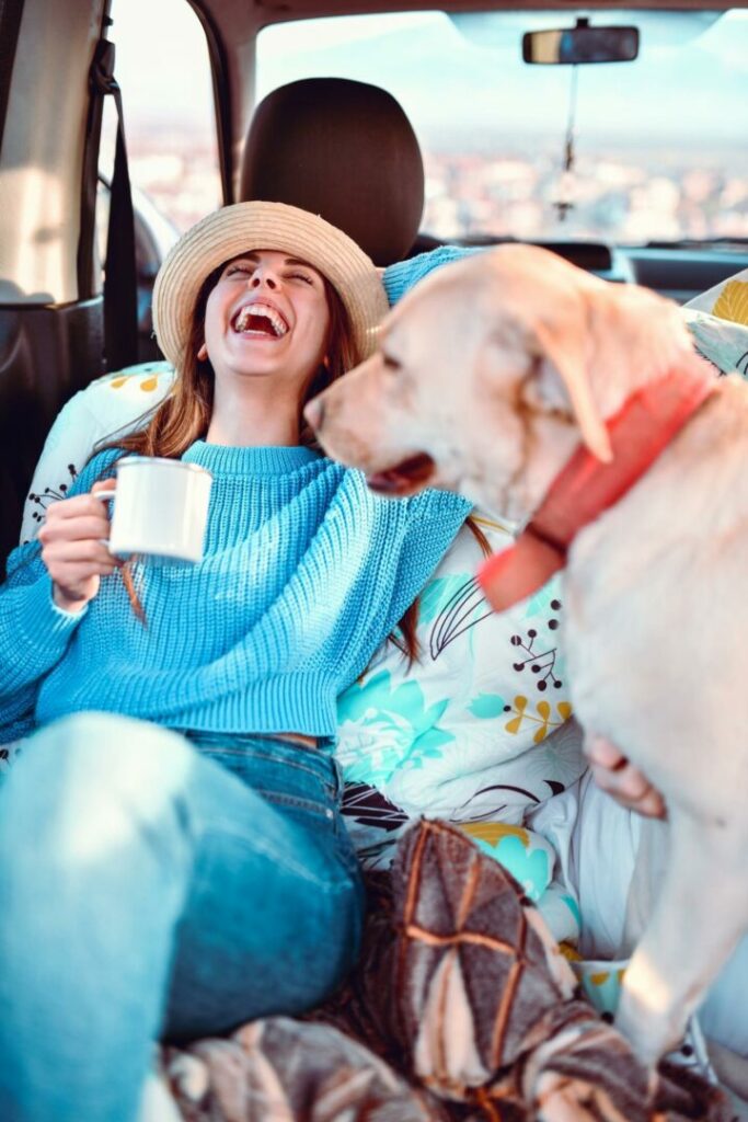 A young woman laughs enthusiastically while petting her dog in the back of an RV