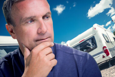 A man ponders who makes Keystone RVs with travel trailers in the background