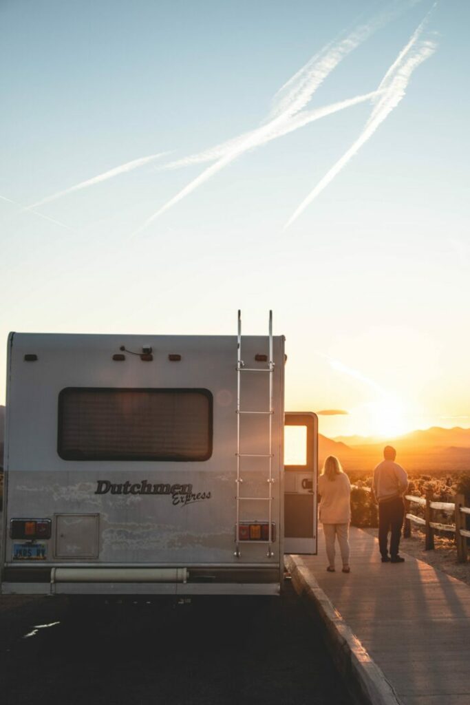 A couple stand beside their Dutchmen RV made, by Keystone RV, to catch the sunset over the mountains