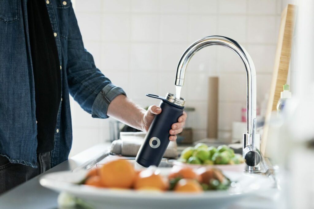 A man fills up a water bottle via the kitchen sink faucet.
