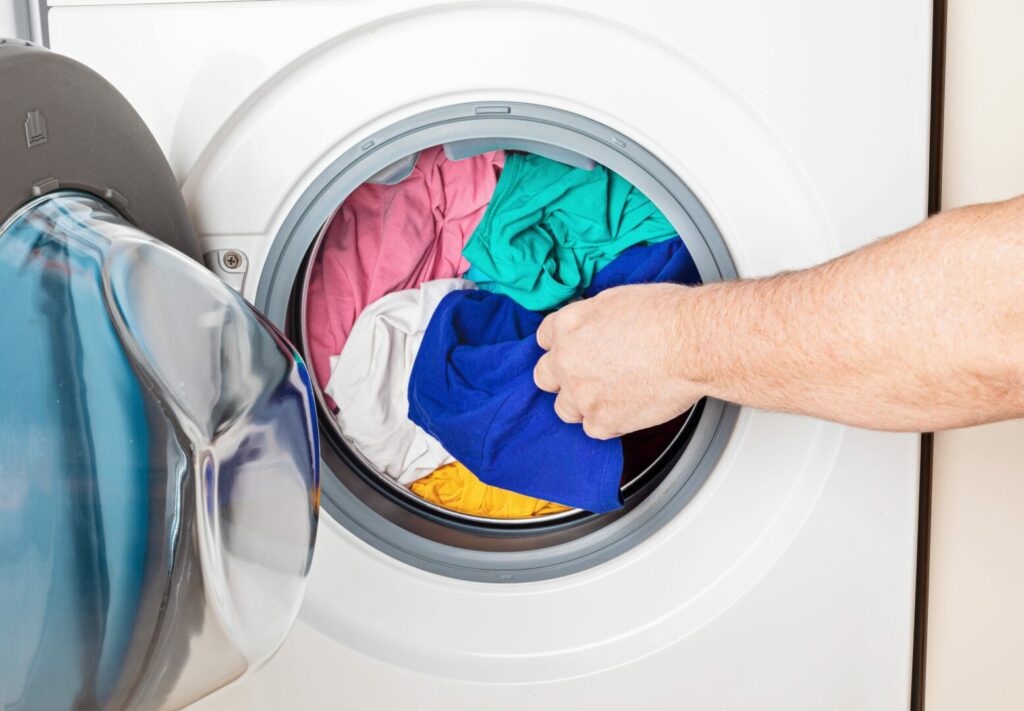 A man's hand loading colorful clothes into an RV washer dryer combo 