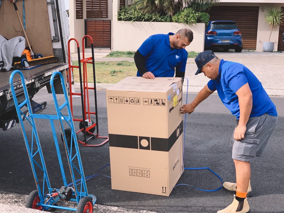 Two couriers unload a large box from a delivery truck.