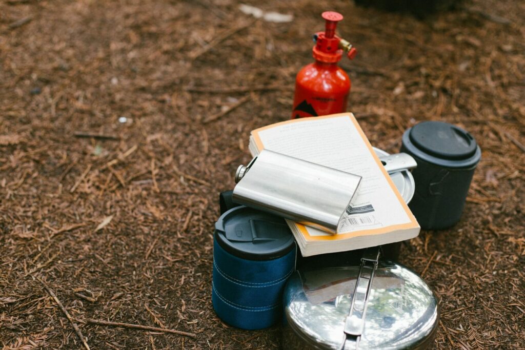 Camping supplies of insulated mugs, pots, and pans gathered on the ground