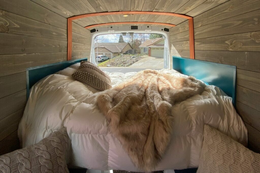 A cozy bed with furry blankets and a down comforter in a camper van.