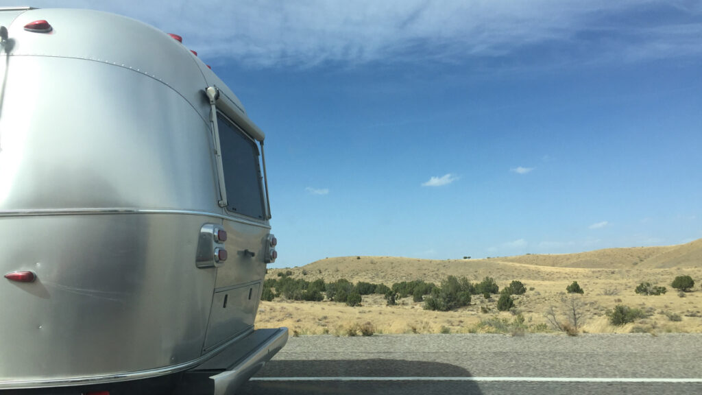The back of a small airstream travel trailer under 5000 lbs driving on the highway.