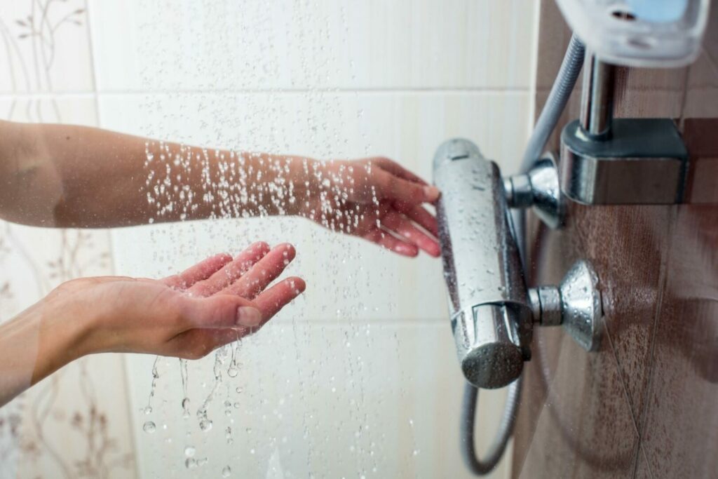 A woman adjusts the temperature of the shower water as it falls from the head.