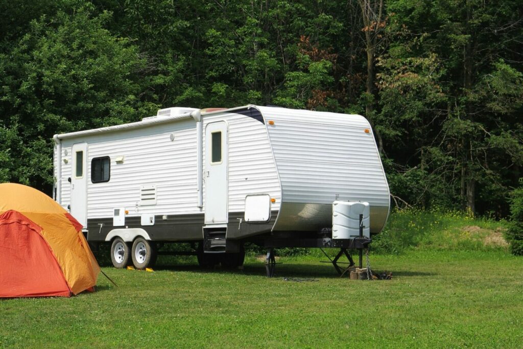 A travel trailer in a nice grassy campsite with a tent set up out front.