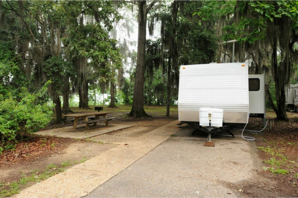 An RV parked on a concrete pad at a campsite with a white propane tank cover.