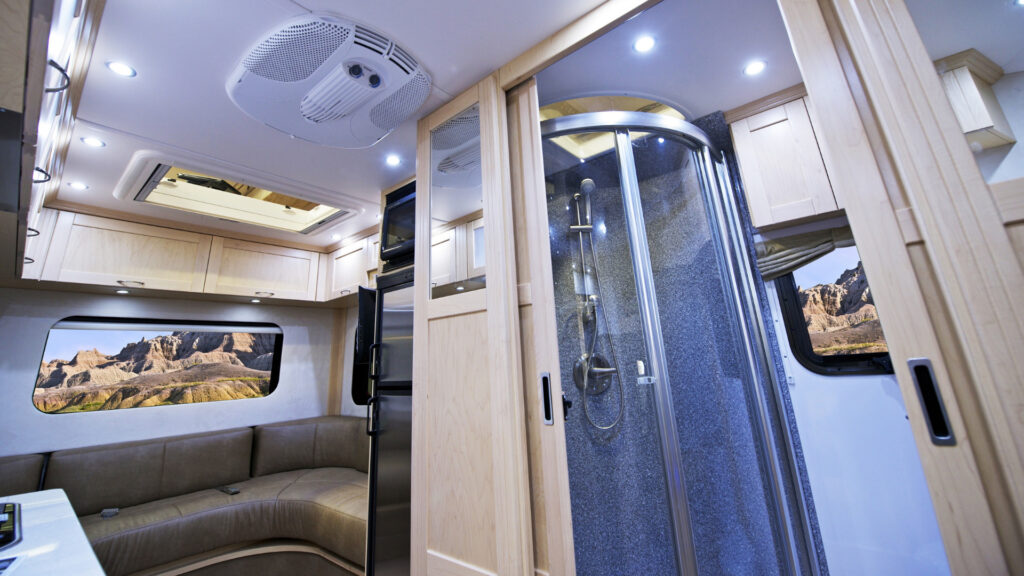 An interior shot of an RV showing the bed and shower. They have on demand hot water because there is an RV tankless water heater installed. 