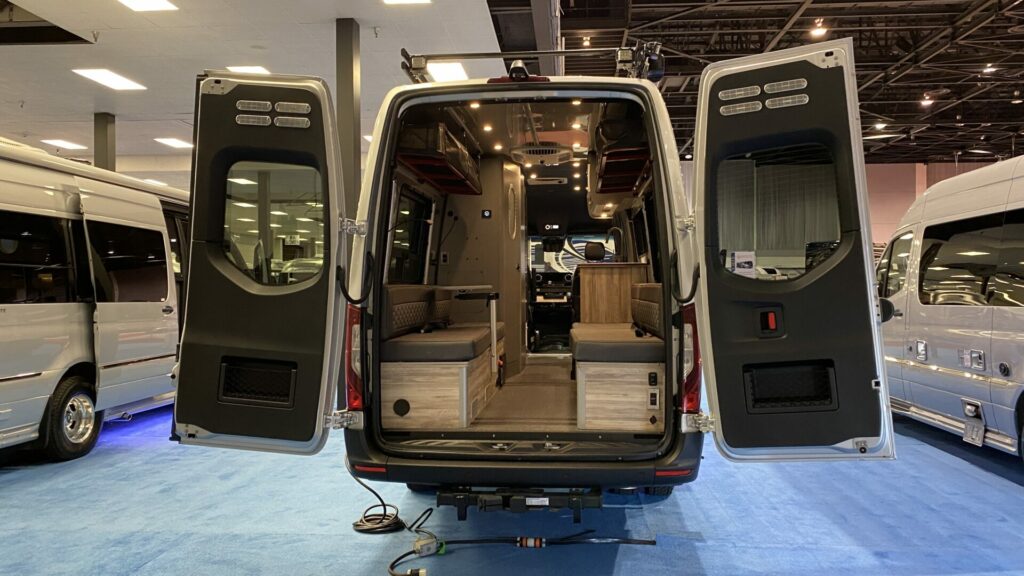 A class B RV with the rear storage doors open to showing you the sitting area inside 