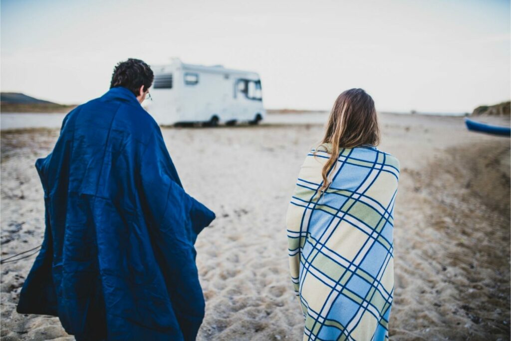 Two campers bundle in blankets to stay warm as they prepare for a freeze at night in their RV.