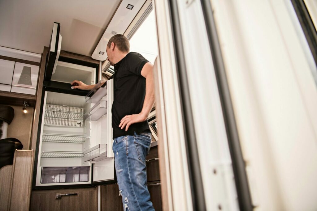 A man adjusts the temperature on an RV fridge with the doors open.