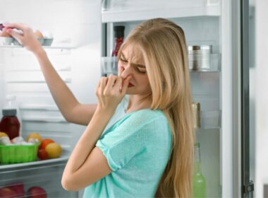 A woman holds her nose to keep from smelling spoiled food as she finds her refrigerator has stopped working.