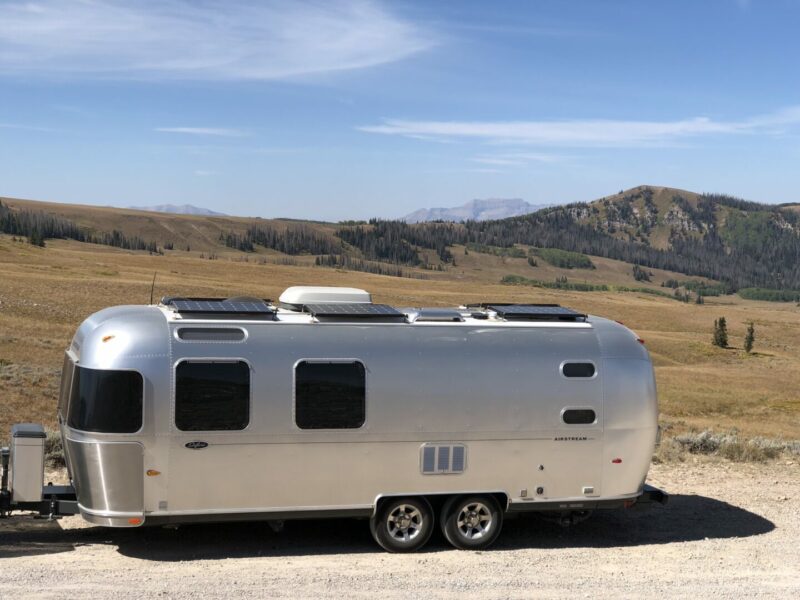 An airstream parked in the desert with solar panels on the roof.