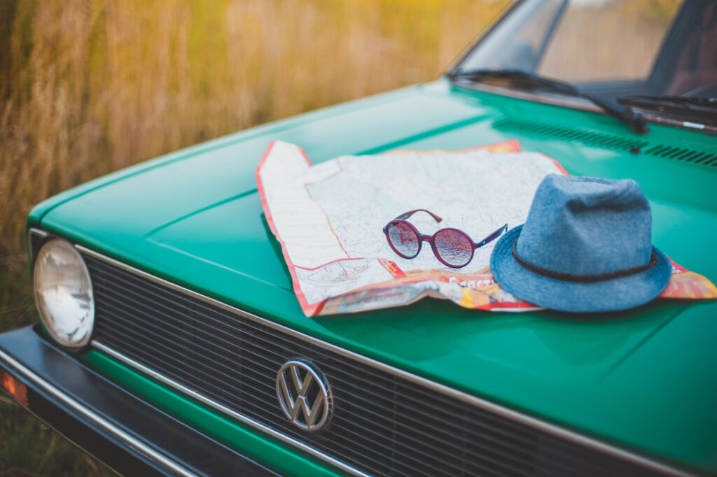 Road trip map and sunglasses sit on the hood of a green car.