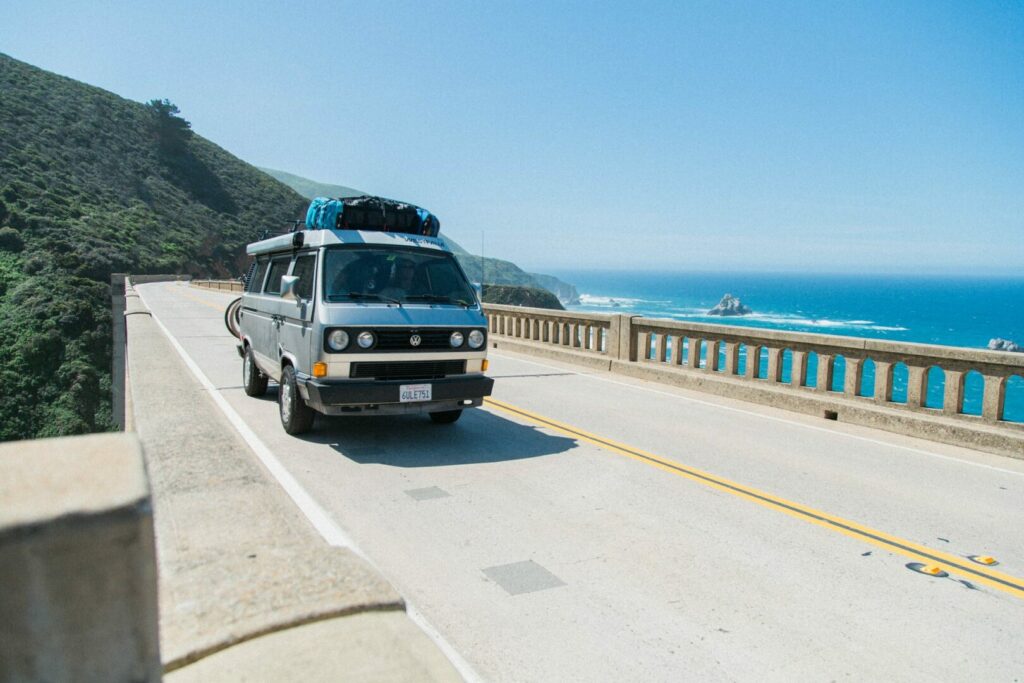 A van drives across Bixby Canyon Bridge in Big Sur on a cross country road trip.