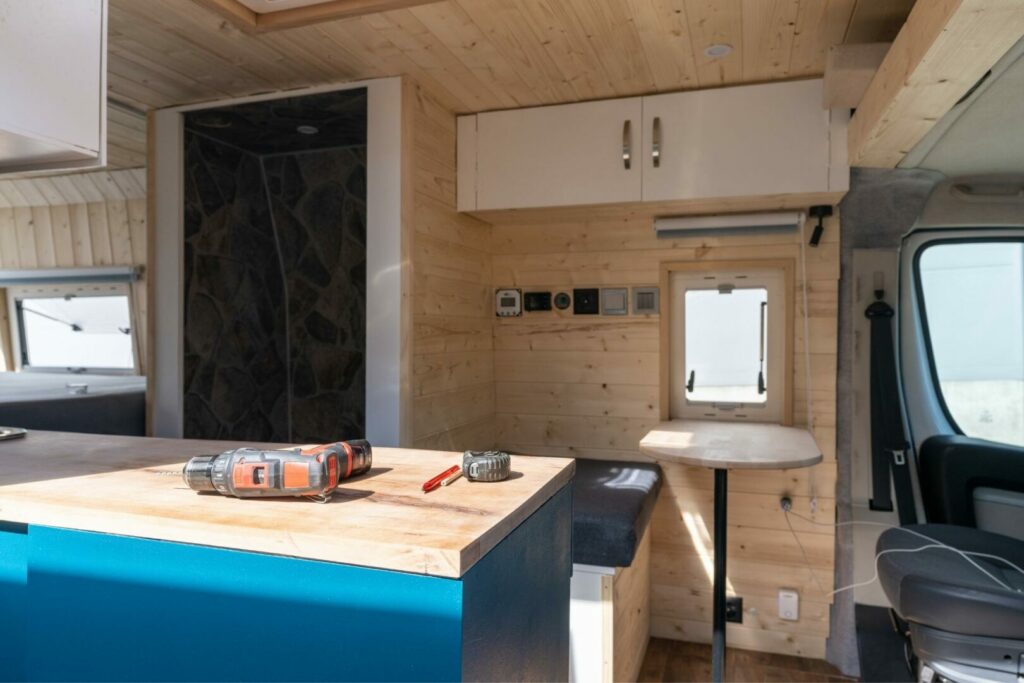 A camp van being built with a dinette behind the driver side seat with a storage bench