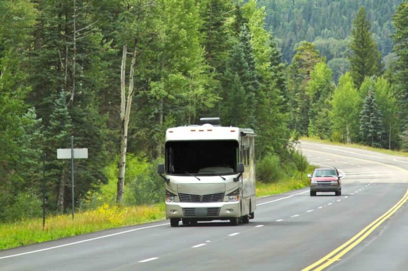 A class a motorhome drives down a highway in a wooded landscape