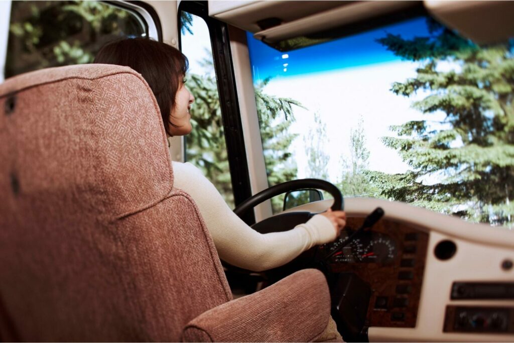 The interior of the front cab of a class a motorhome as a woman drives down the road.