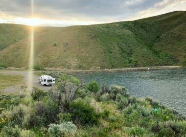 A fifth wheel parked in a remote spot in the mountains near a small lake to enjoy the beautiful outdoors.