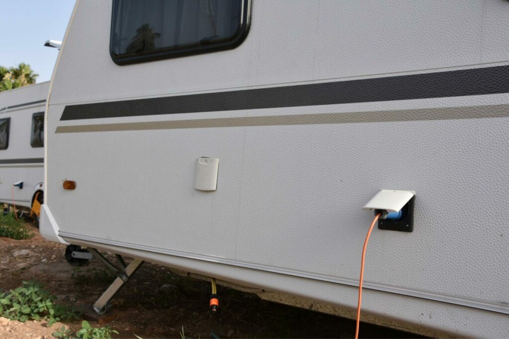 The exterior side of an RV with a power cord plugged into the connection point.