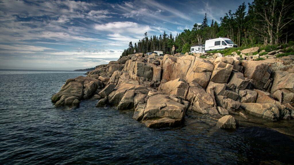 A campervan and other RV parked along the rocky coast of the ocean for scenic camping.