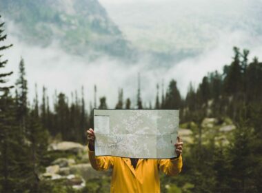 A camper holds up a map as they traverse through a forested, mountain region.