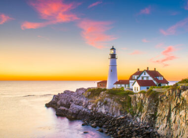 A lighthouse on the coast in Maine shines agains a colorful sunset.