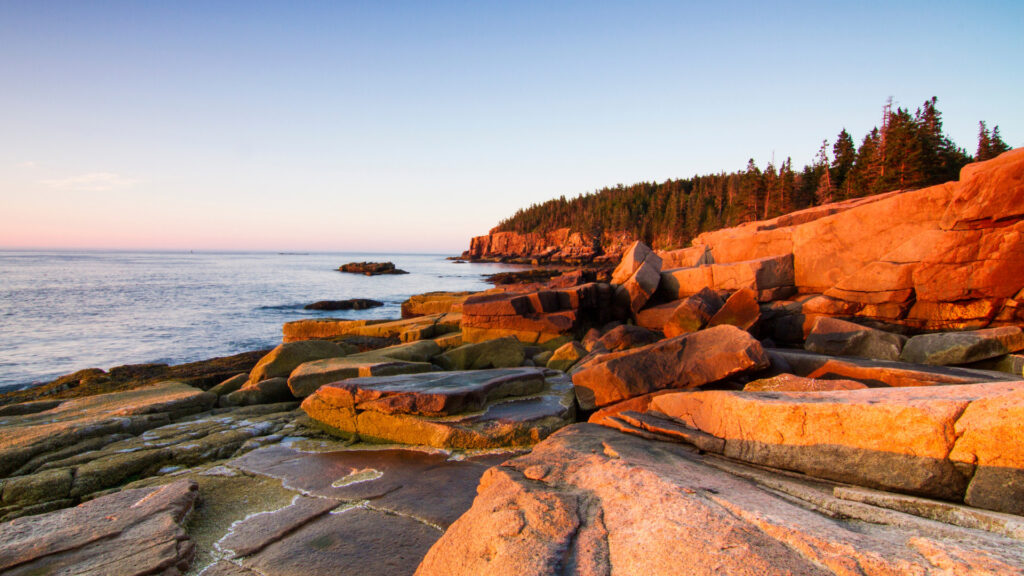 The coastline of Acadia National Park in Maine glows in a rosy sunset light.