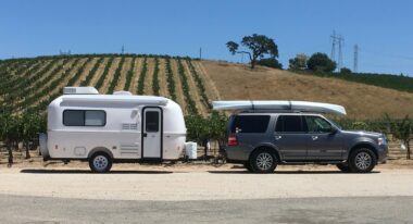 A Casitas Camper being towed in front of a winery vineyard by an SUV with a canoe on the roof.