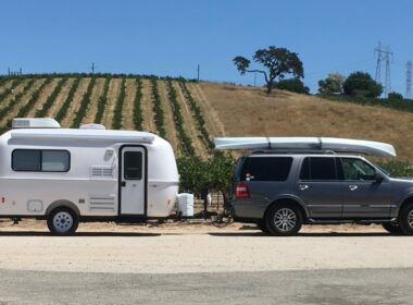 A Casitas Camper being towed in front of a winery vineyard by an SUV with a canoe on the roof.