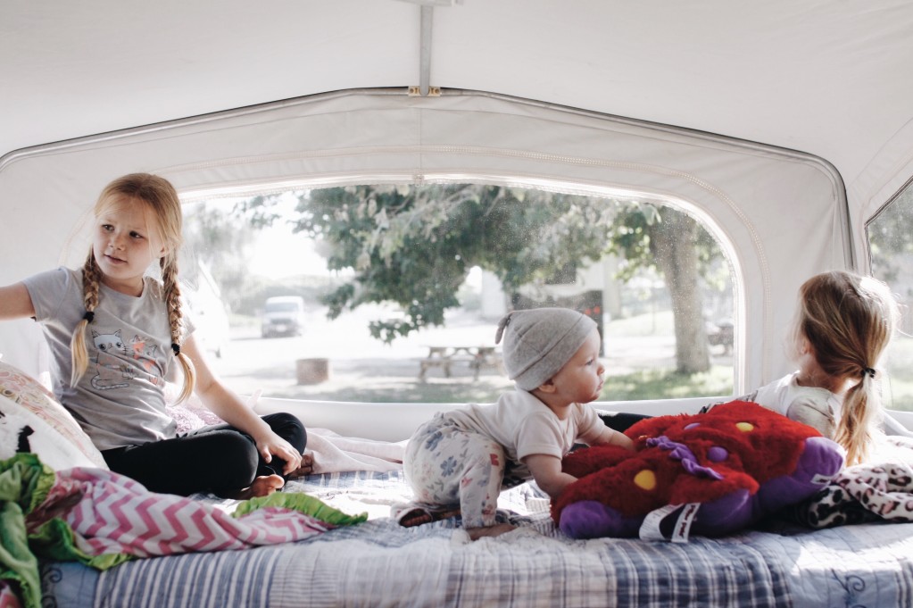 Three small kids play on the bunk inside of an RV.
