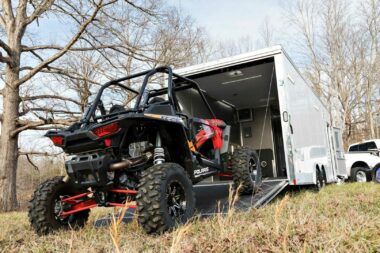 An ATV drives into a toy hauler parked in a field.