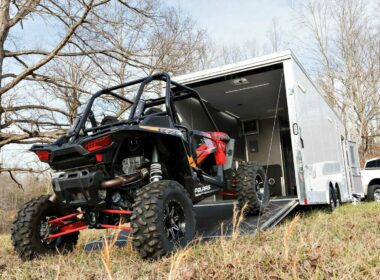 An ATV drives into a toy hauler parked in a field.