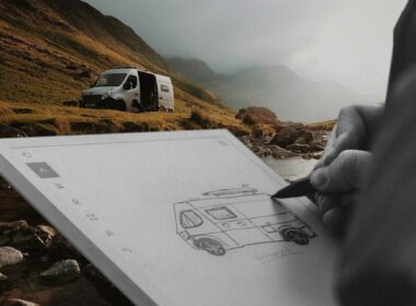 Drawing a conceptual van on a notepad with a class b van camping in the distance near a stream