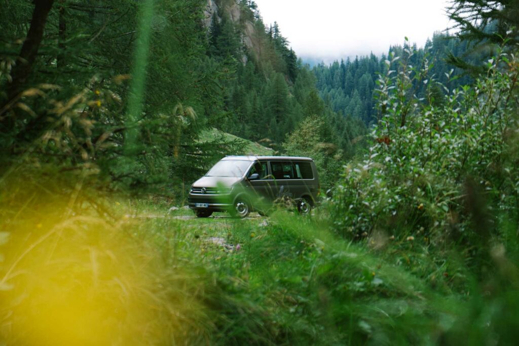 A green camper van parked on a trail through the woods.