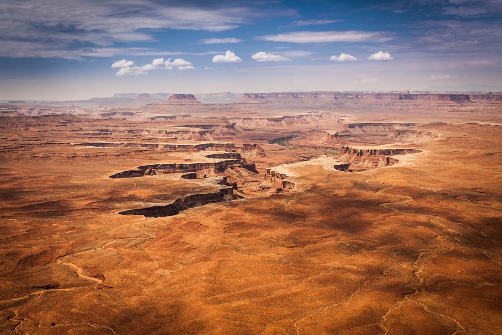 Looking over flat landscape to see vast canyons cutting across the Earth's surface in Canyonlands National Park, UT