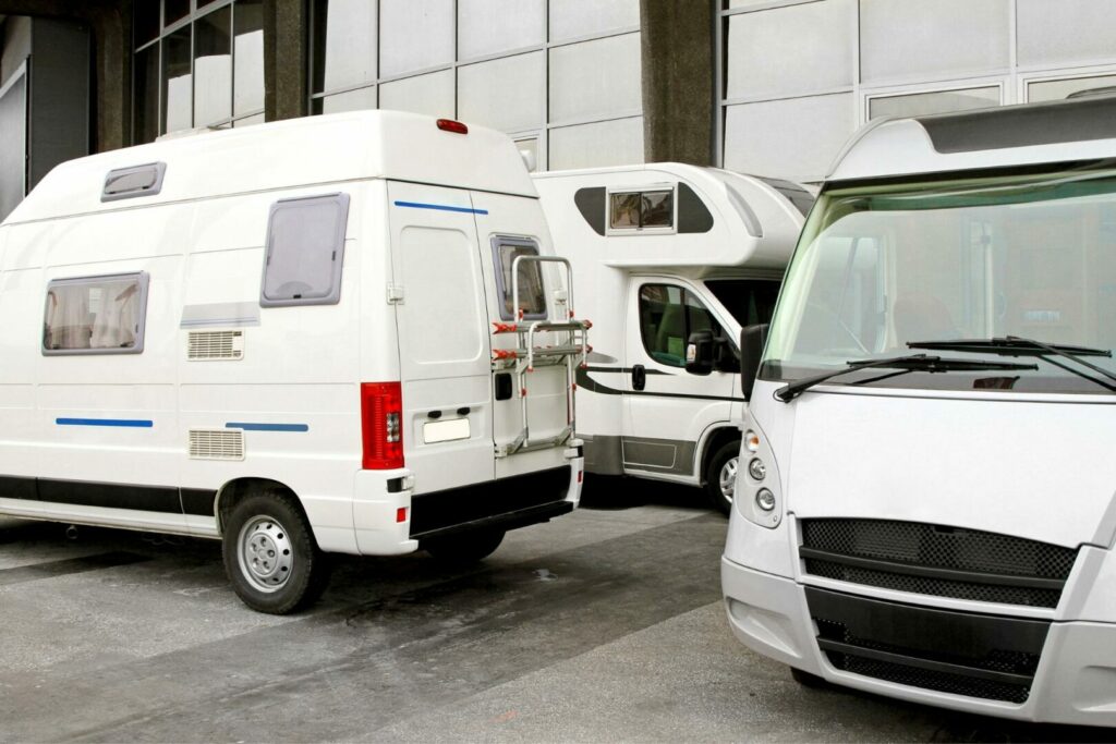 Two class B vans and a Class C motorhome parked outside a dealership entrace.
