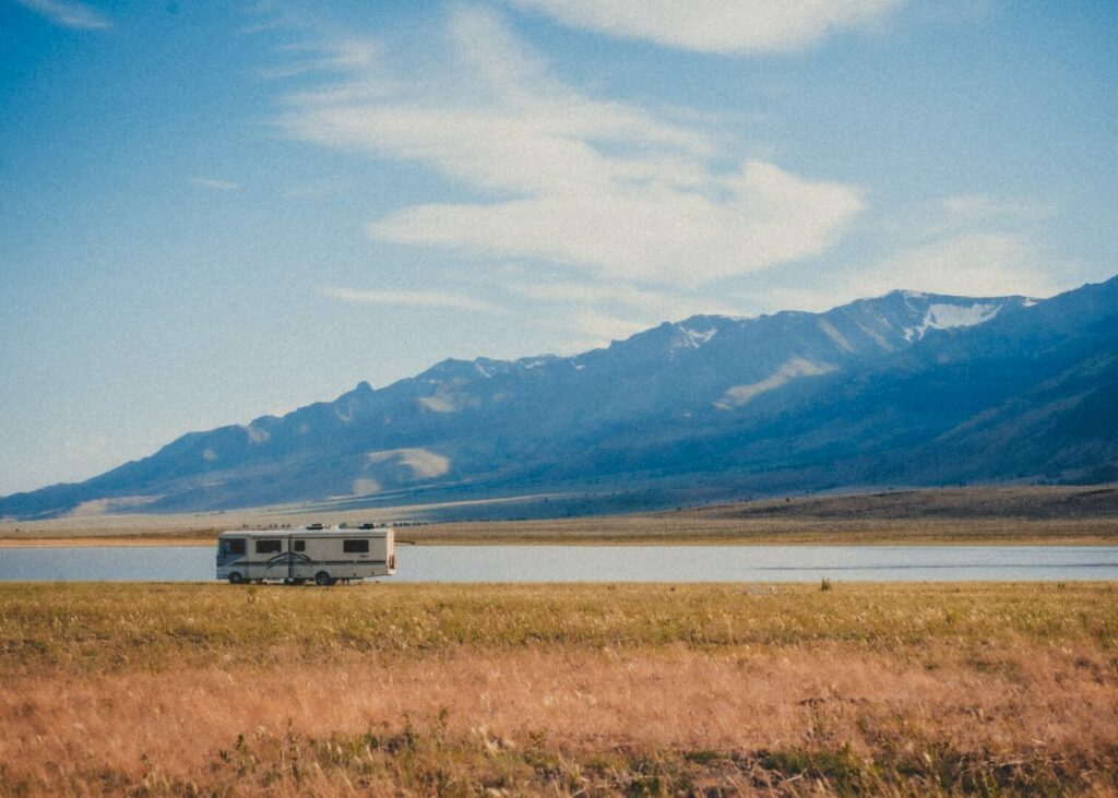 An RV dispersed camping in a yellow field with towering mountains in the distance.