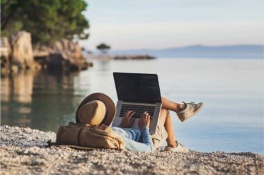 A man relaxes on a beach near the water and checks his mail on his computer.
