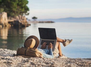 A man relaxes on a beach near the water and checks his mail on his computer.