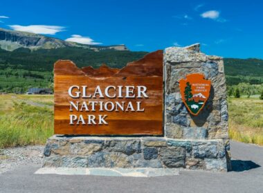 A sign outside of Glacier National Park made of wood and stone and sporting the National Park Service logo.